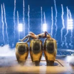Karol G lies across gold conga drums under pyrotechnics at MetLife Stadium